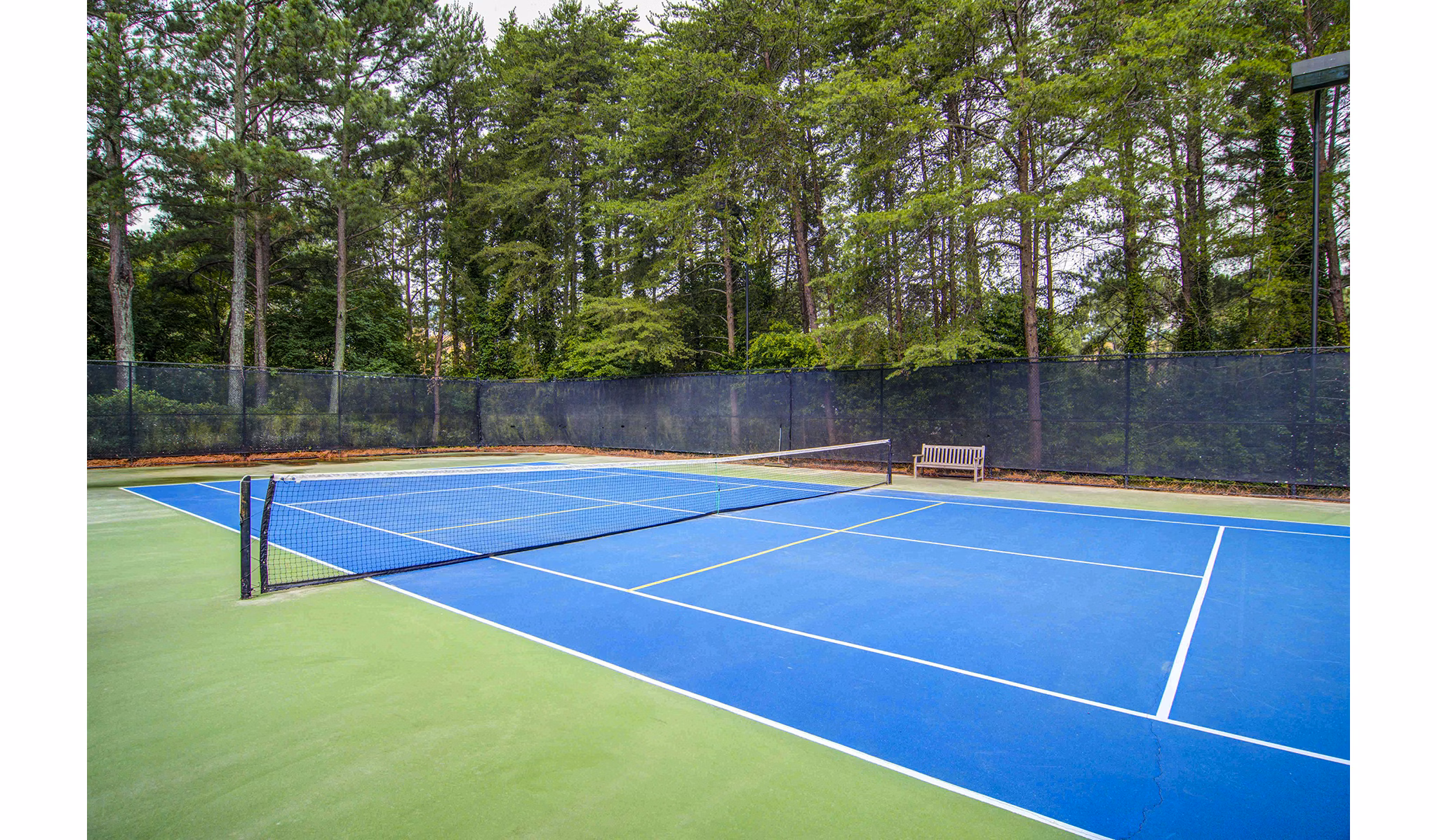 Tennis court with bright green surface at The Prato at Midtown Apartments, offering a premium sports experience in a luxury setting