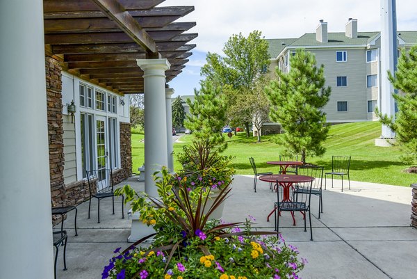 Outdoor patio with tables and chairs surrounded by potted plants at luxury apartments Trees and a building are in the background