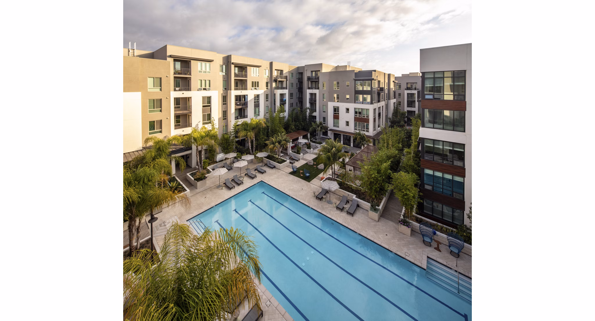Luxury swimming pool at One Paseo Living Apartments featuring sleek lounge chairs and palm trees, perfect for relaxation and recreation