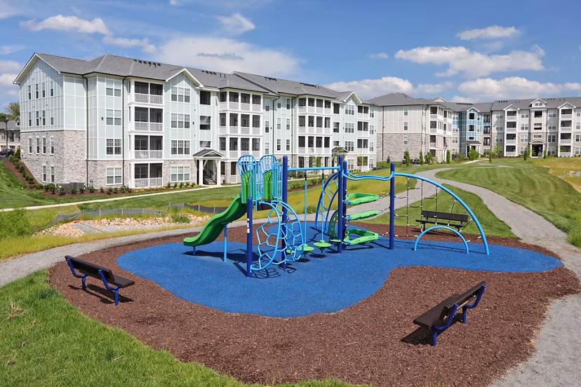 Colorful playground surrounded by trees at Avia Apartments, offering a fun and safe environment for families