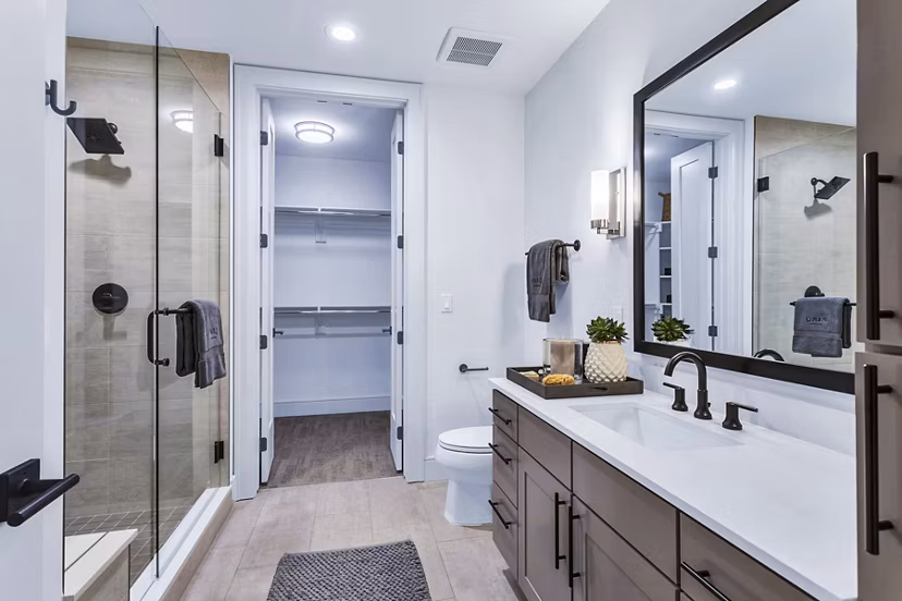 Sleek bathroom with glass shower, large mirror, and walk-in closet at Parq on Speer Apartments in Denver, offering modern luxury living