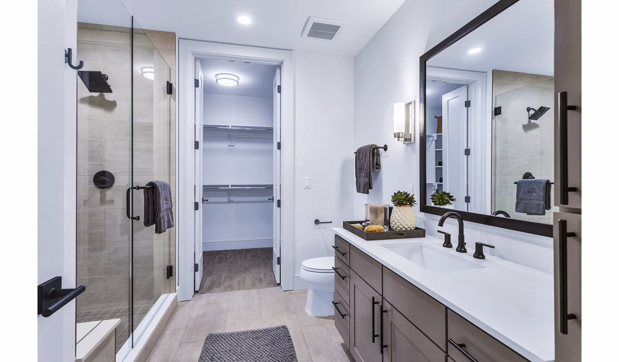 Sleek bathroom with glass shower, large mirror, and walk-in closet at Parq on Speer Apartments in Denver, offering modern luxury living