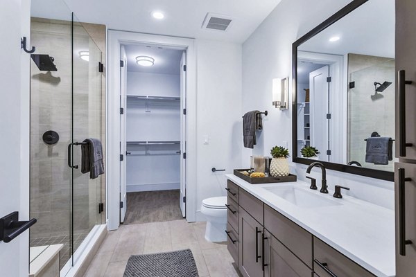 Sleek bathroom with glass shower, large mirror, and walk-in closet at Parq on Speer Apartments in Denver, offering modern luxury living