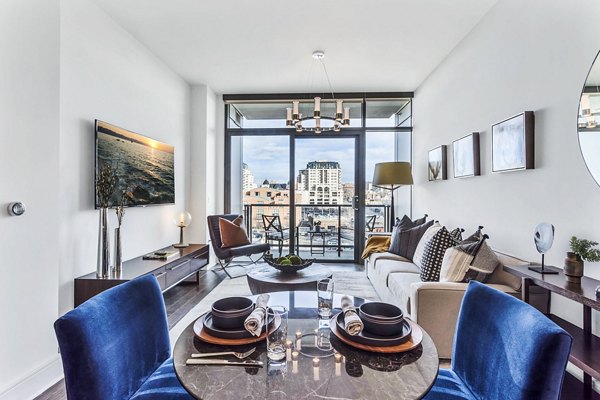 Parq on Speer Apartments: Bright living room with blue chairs, city view, and dining table in luxury Denver apartments