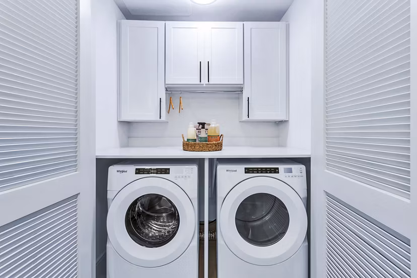 Compact laundry room featuring washer, dryer, and storage cabinets in Parq on Speer Apartments, luxury living in Denver