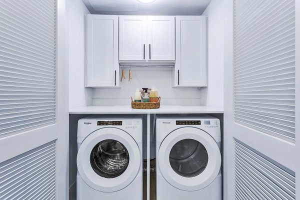 Compact laundry room featuring washer, dryer, and storage cabinets in Parq on Speer Apartments, luxury living in Denver