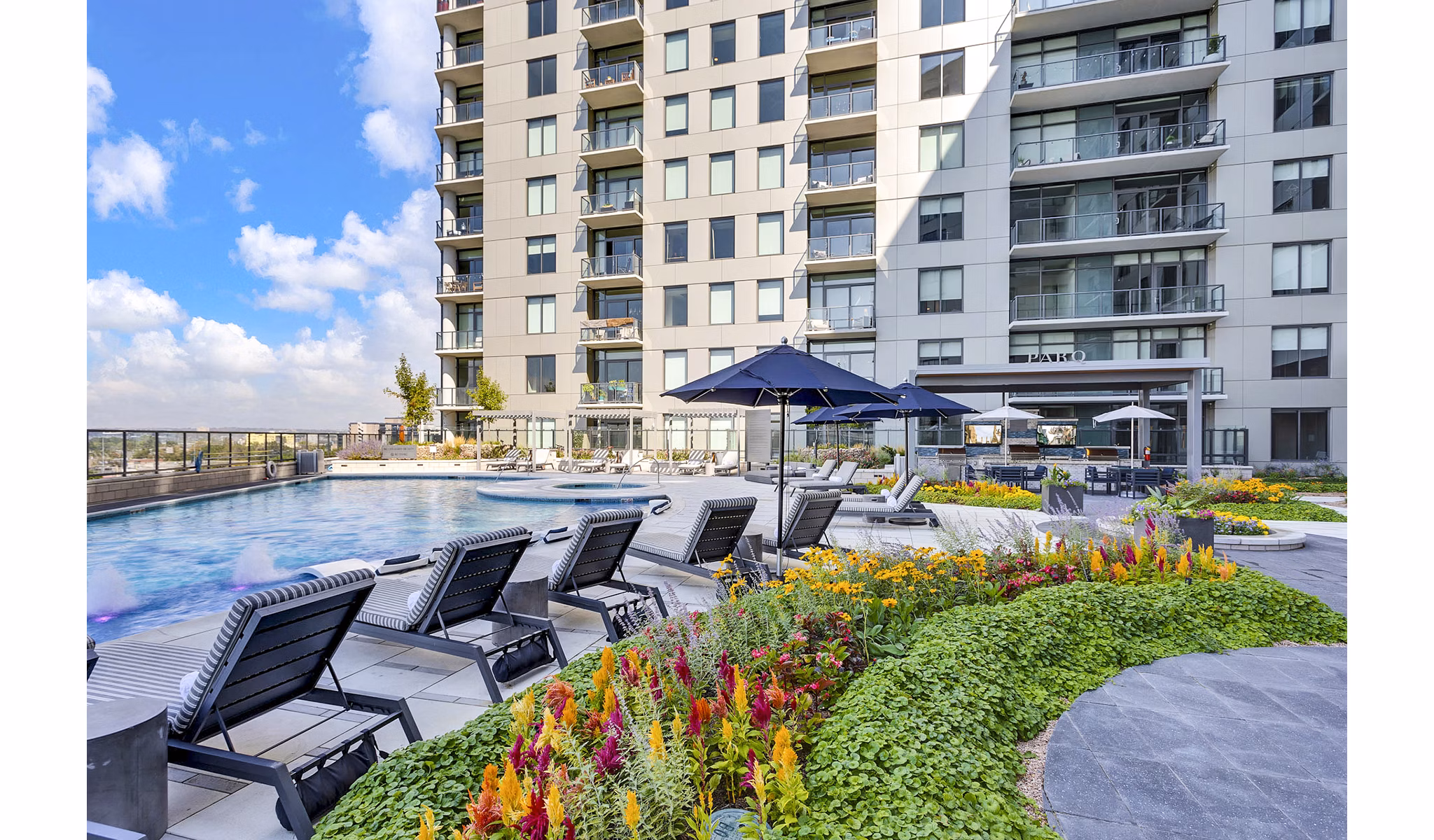 Parq on Speer: Luxury apartment building with pool, lounge chairs, and vibrant flowers in Denver