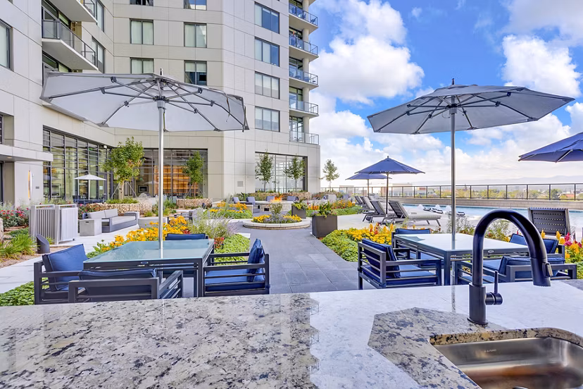 Outdoor patio with tables and umbrellas by garden at Parq on Speer: Luxury high-rise apartments in downtown Denver