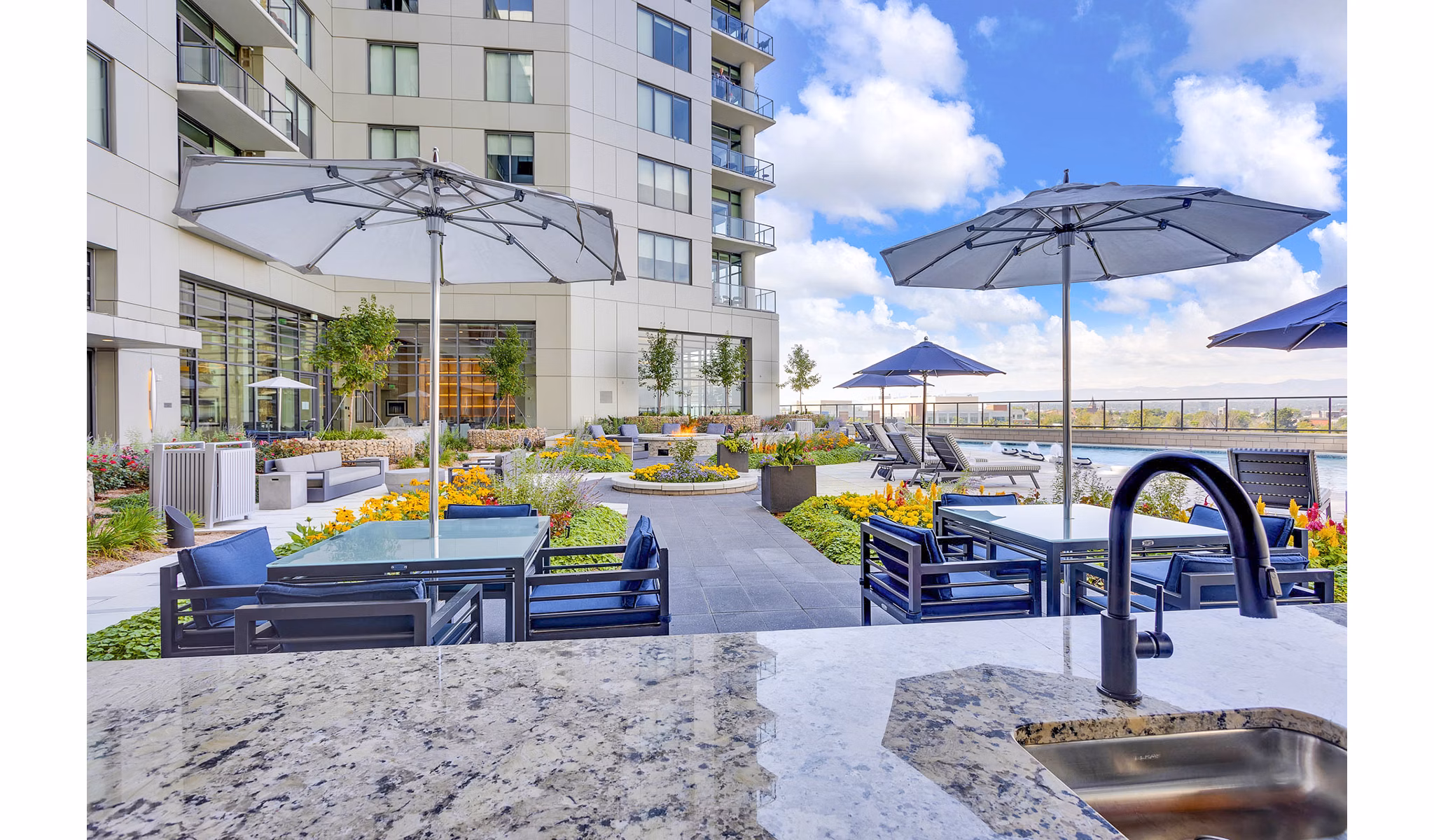 Outdoor patio with tables and umbrellas by garden at Parq on Speer: Luxury high-rise apartments in downtown Denver