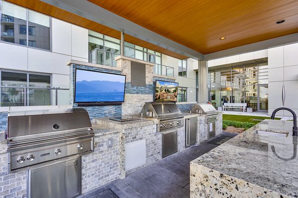 Outdoor kitchen with stainless steel grills and mounted TVs at Parq on Speer Apartments, luxury living offered by Greystar