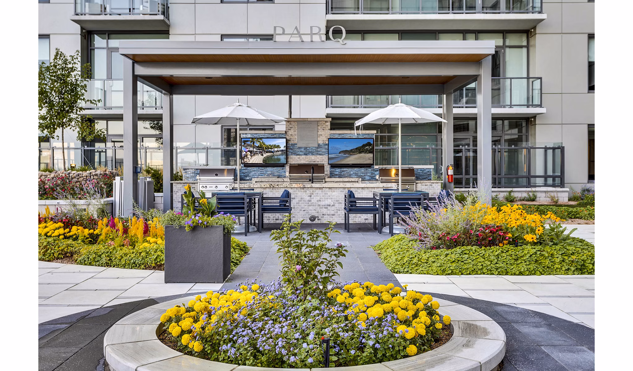 Modern outdoor patio with seating, umbrellas, and vibrant flowers at Parq on Speer Apartments, a luxury  property
