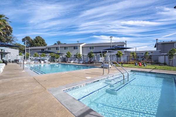 Relaxing pool area at Admirals Cove Apartments featuring lounge chairs and lush landscaping, perfect for unwinding in a serene environment