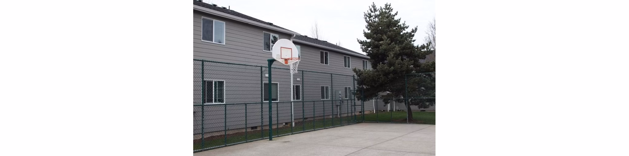 Outdoor sport court at Village East Apartments with basketball hoops and tennis markings, offering recreational amenities for residents