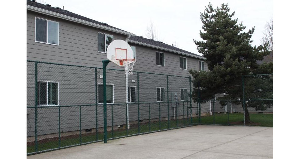 Outdoor sport court at Village East Apartments with basketball hoops and tennis markings, offering recreational amenities for residents