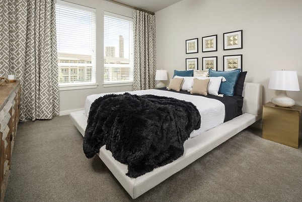 Cozy bedroom with neutral tones and large windows at The Upton at Longhorn Quarry Apartments
