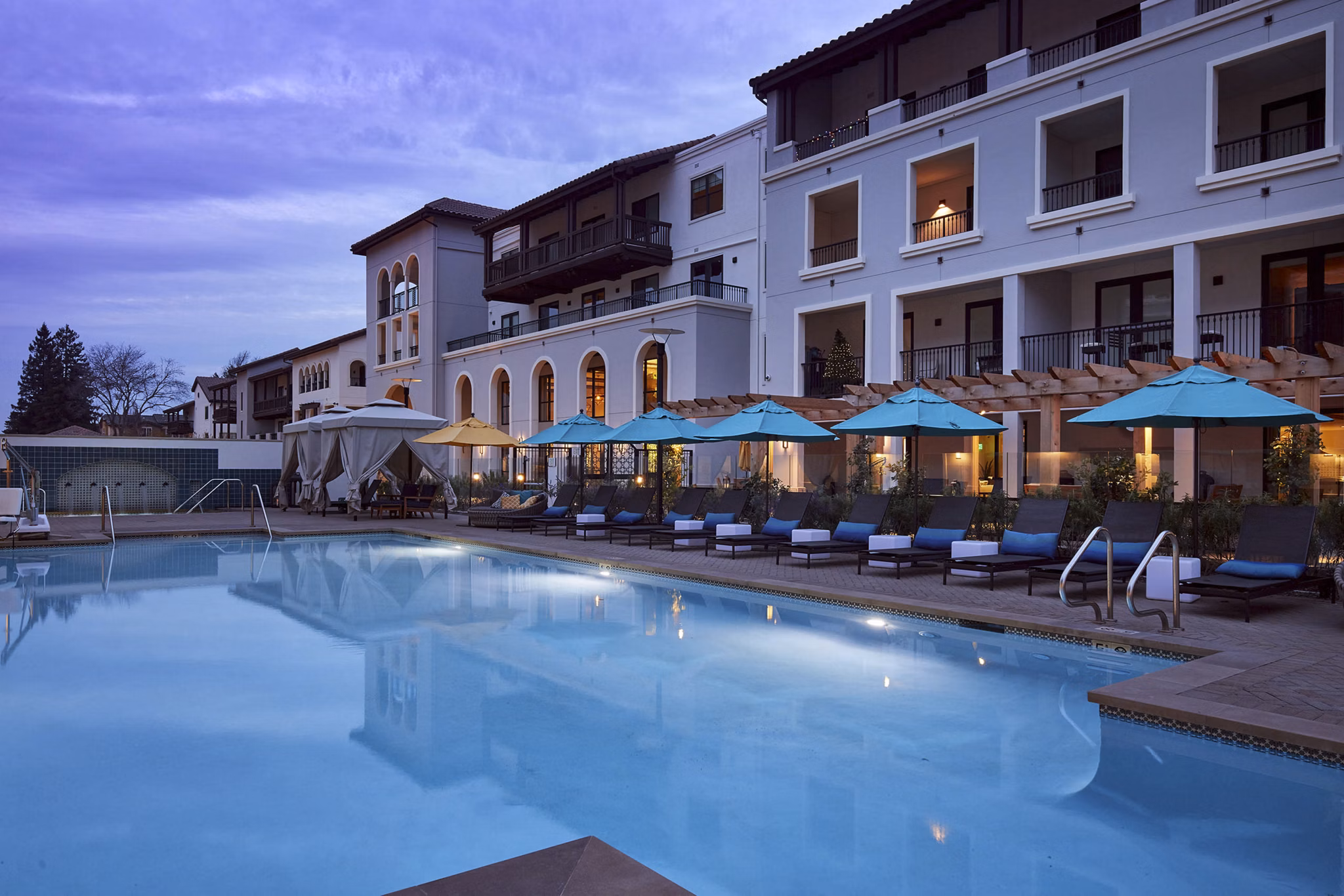 Nighttime swimming pool area with hot tub, outdoor fireplace, and seating at luxury apartments