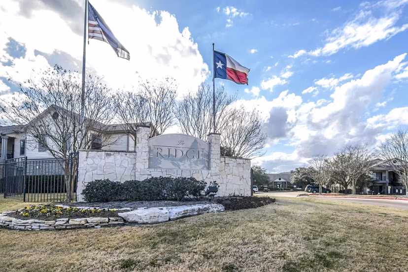 Ridge entrance stone sign with vibrant landscaping and flags in front of luxury apartments