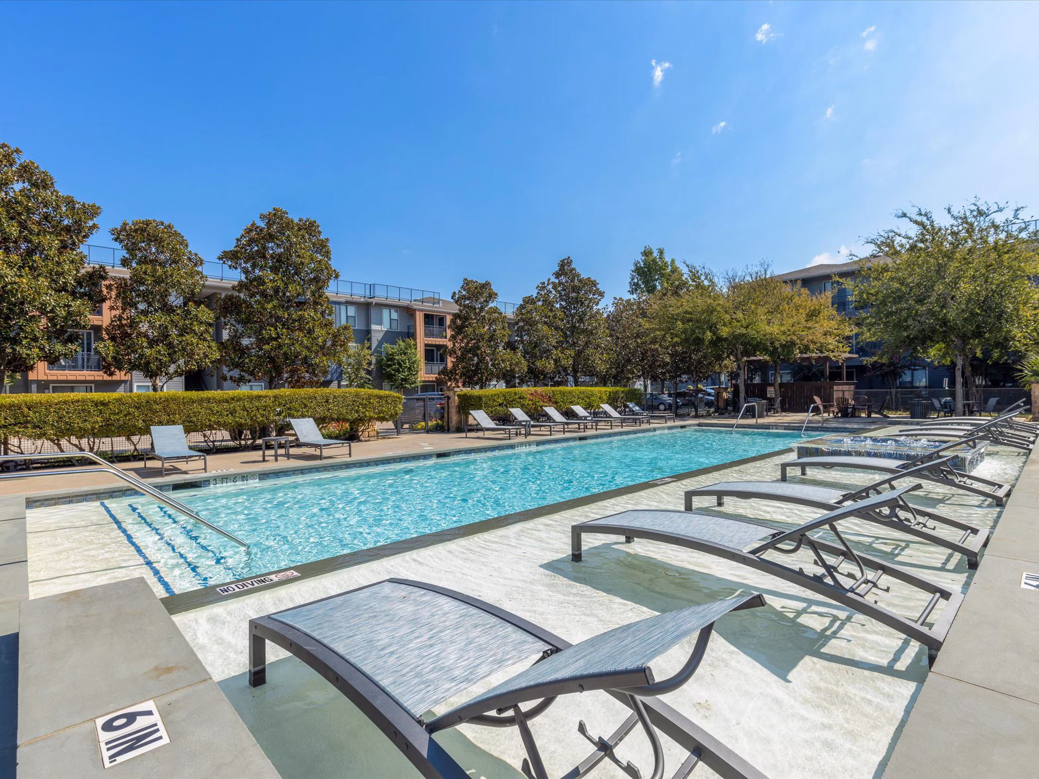 Poolside relaxation area at The Avery on Southwestern apartments, featuring luxury amenities like chaise lounges and water views for residents