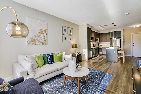 Modern living room and kitchen with white sofa, colorful cushions, and stainless steel appliances in luxury apartments