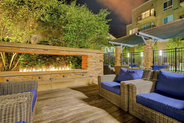 Outdoor seating area with wicker furniture and a fire feature surrounded by greenery at luxury apartments