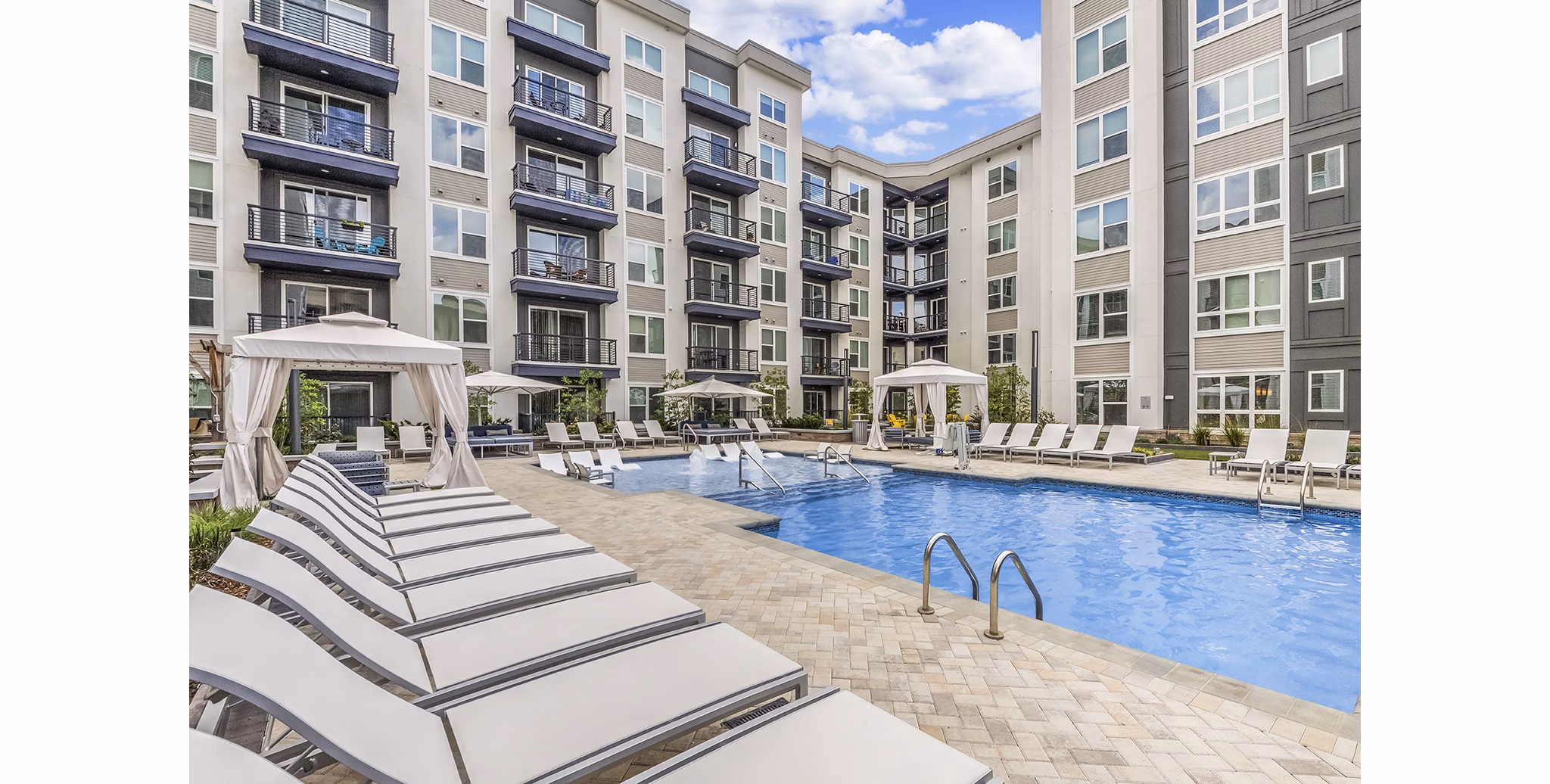 Sunlit outdoor pool surrounded by lush landscaping at Bainbridge South End Apartments