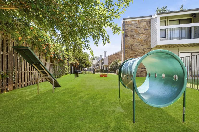 Spacious enclosed dog park with agility equipment at Woodland Trails Apartments, offering a pet-friendly environment for residents