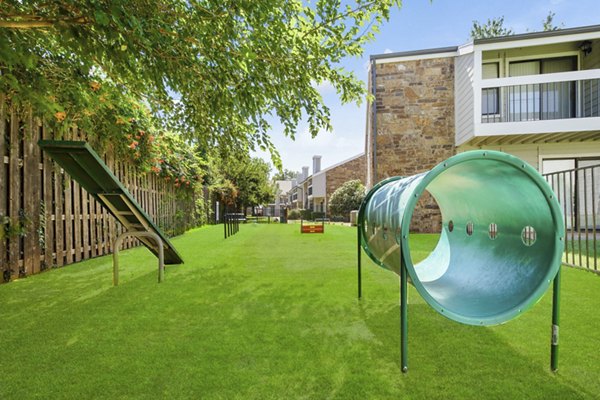 Spacious enclosed dog park with agility equipment at Woodland Trails Apartments, offering a pet-friendly environment for residents