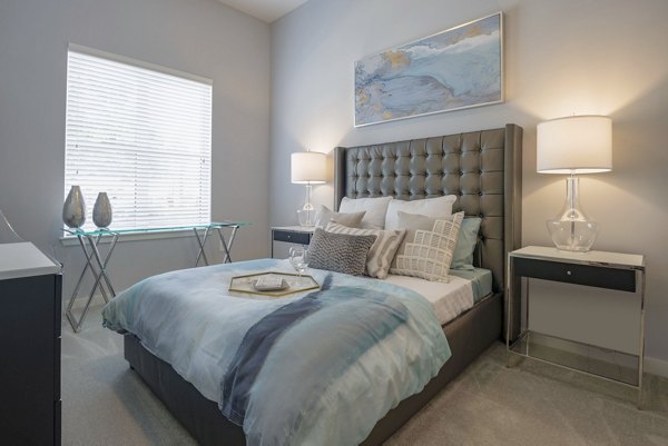 Cozy bedroom with modern decor at Aston City Springs Apartments, featuring plush bedding and ample natural light