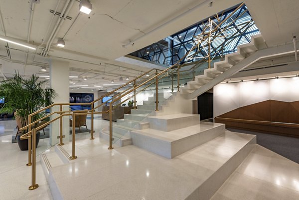 Modern interior space featuring a staircase with glass railings and plants, illuminated by a skylight