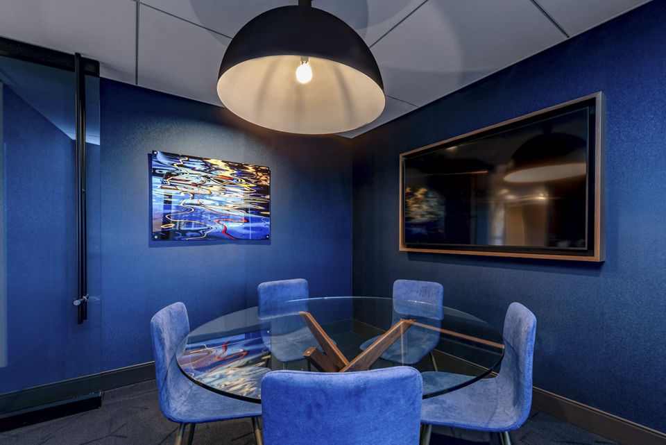 Modern meeting room featuring a round glass table and blue chairs with pendant lighting and wall art