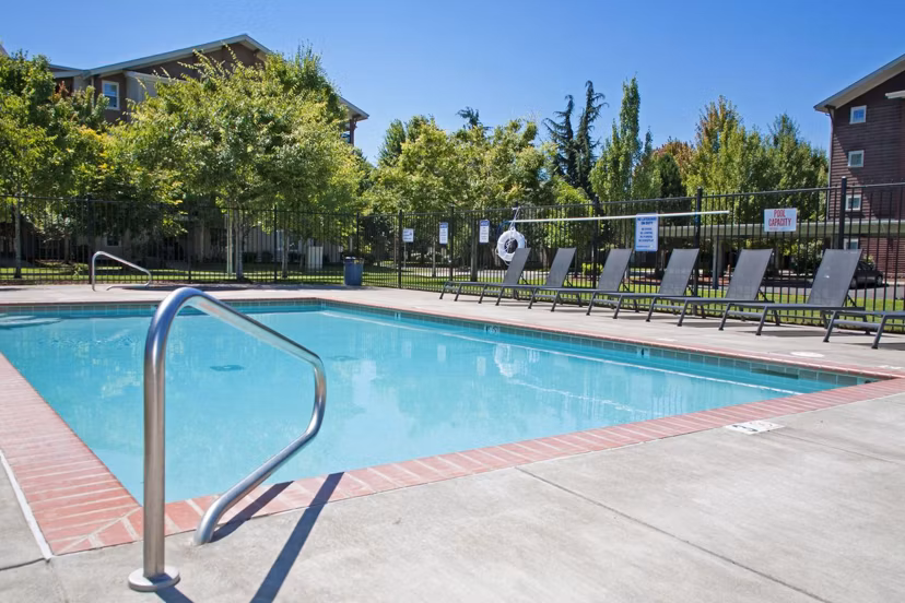 Resort-style outdoor pool at Willamette Gardens Apartments, featuring lush landscaping and comfortable lounge chairs