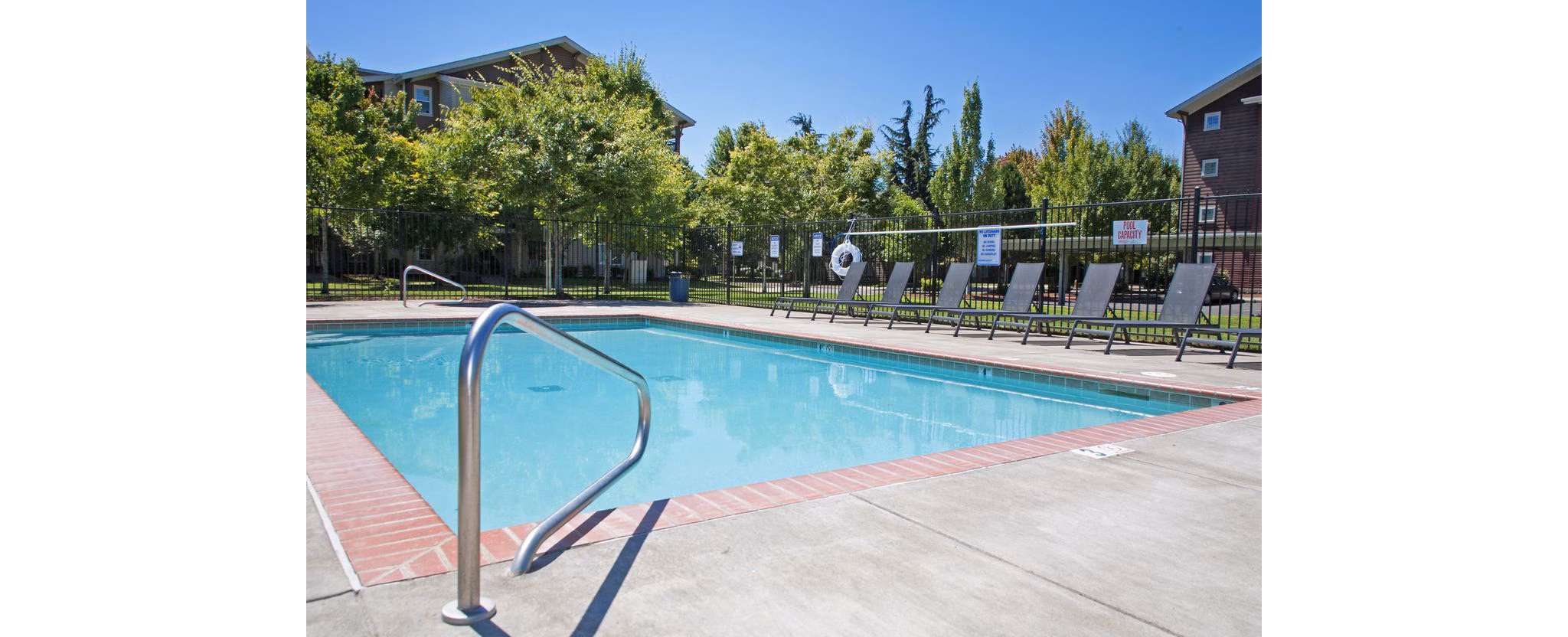 Resort-style outdoor pool at Willamette Gardens Apartments, featuring lush landscaping and comfortable lounge chairs