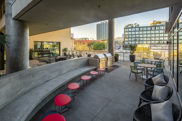 Grill area with seating at Rise Hollywood Apartments, featuring stainless steel BBQs and shaded picnic tables for outdoor dining