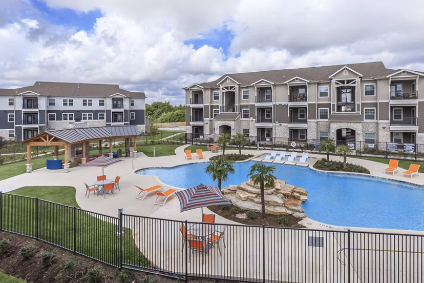 Relaxing pool area at Roots at Waco Apartments featuring modern lounge chairs and lush landscaping