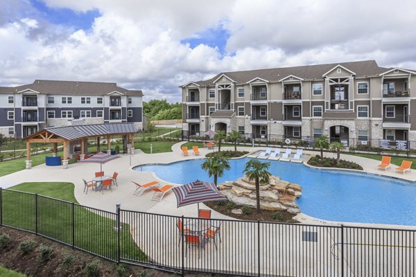 Relaxing pool area at Roots at Waco Apartments featuring modern lounge chairs and lush landscaping