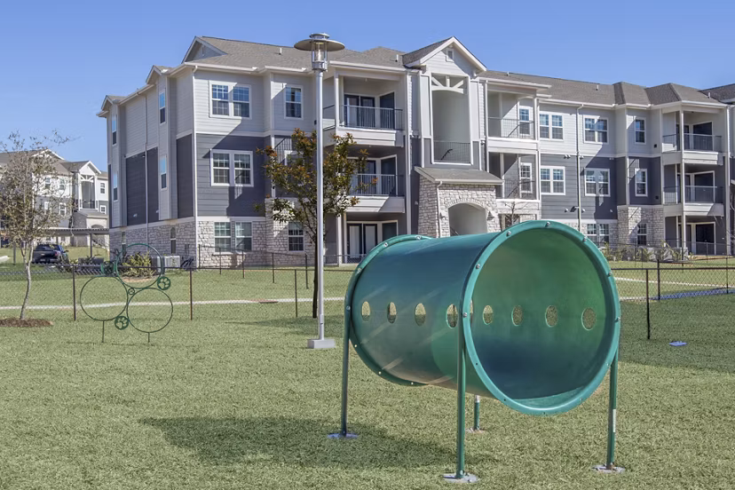 Dog park with agility equipment and shaded seating at Roots at Waco Apartments, providing a fun outdoor space for residents' pets