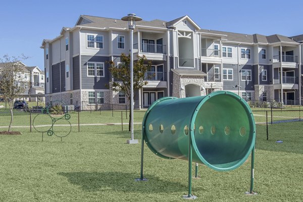 Dog park with agility equipment and shaded seating at Roots at Waco Apartments, providing a fun outdoor space for residents' pets