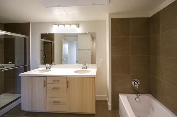 Modern bathroom featuring a double sink vanity, large mirror, bathtub, and shower in luxury apartment