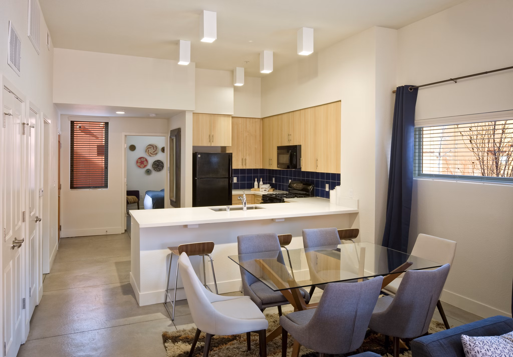 Modern kitchen and dining area with light wood cabinets and glass table in luxury apartment