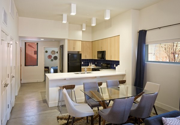 Modern kitchen and dining area with light wood cabinets and glass table in luxury apartment