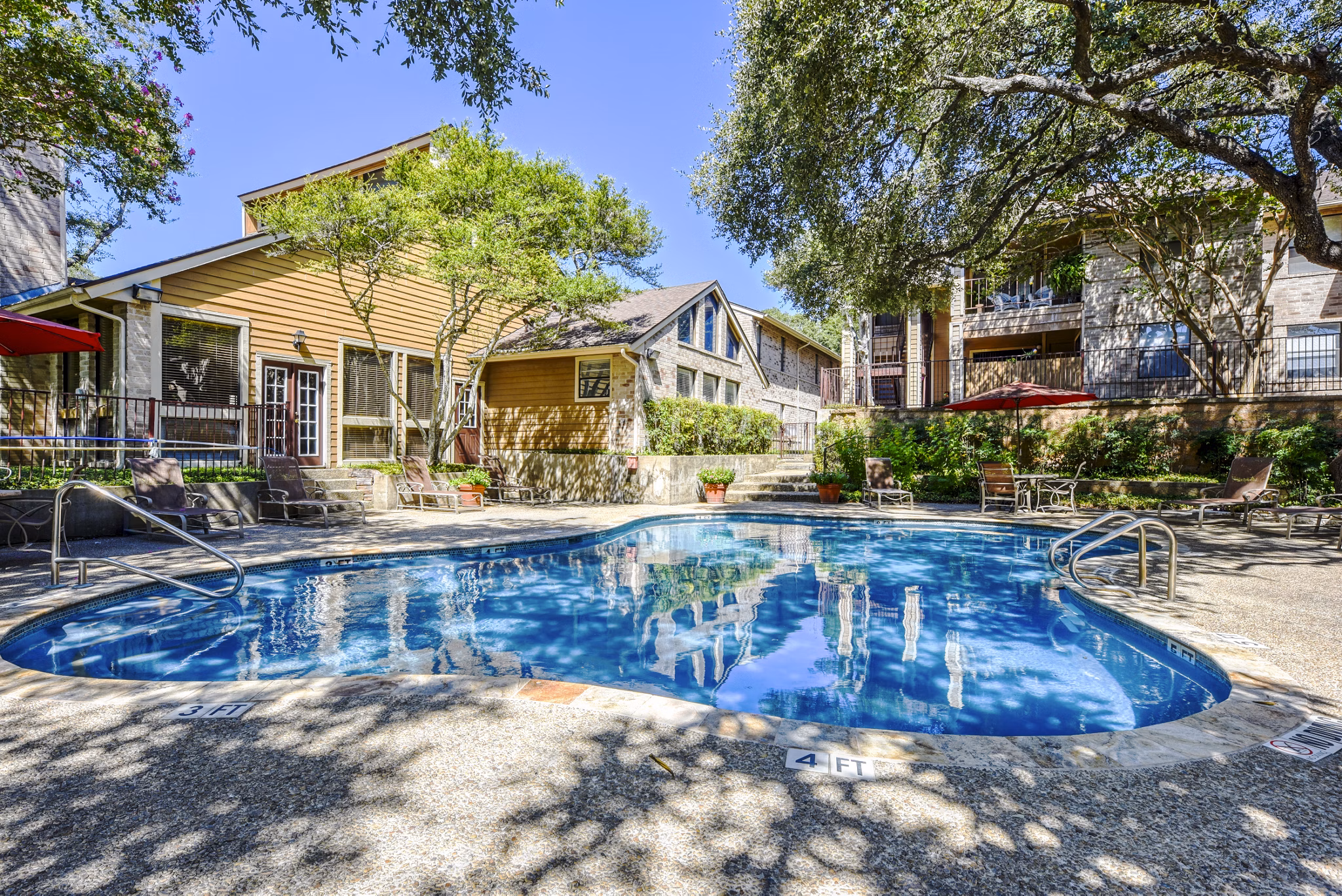 Outdoor pool area with sun loungers at Woods of Elm Creek Apartments, featuring lush greenery and serene vibes, perfect for relaxation