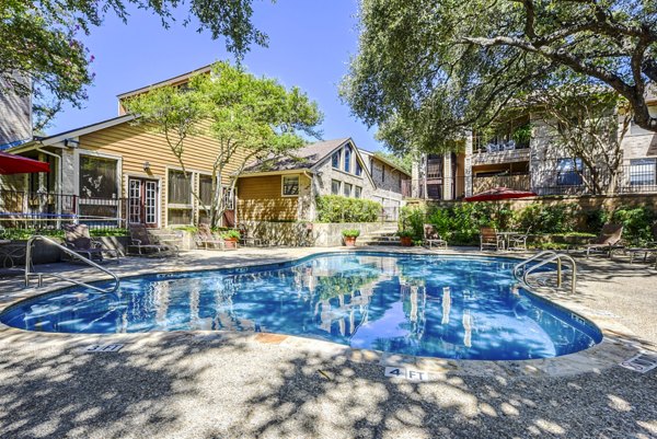 Outdoor pool area with sun loungers at Woods of Elm Creek Apartments, featuring lush greenery and serene vibes, perfect for relaxation