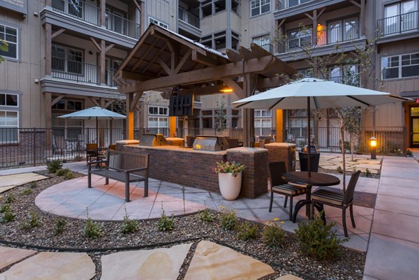 Grill area at Village at Aspen Place Apartments with outdoor seating and lush landscaping