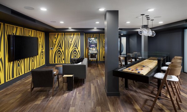 Modern game room featuring a shuffleboard table and seating area with pinball machine in luxury apartments