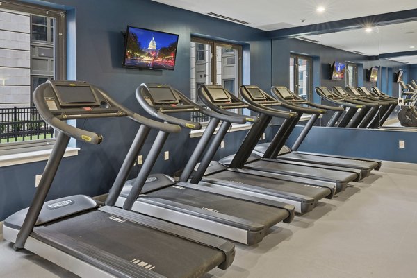 Fitness room with modern equipment at The Quincy Apartments, featuring elliptical machines and free weights for a comprehensive workout experience