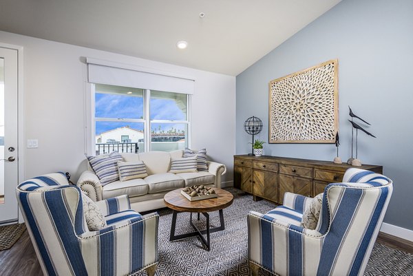 Cozy living room with bay windows and beach-themed decor at Portside Ventura Harbor Apartments