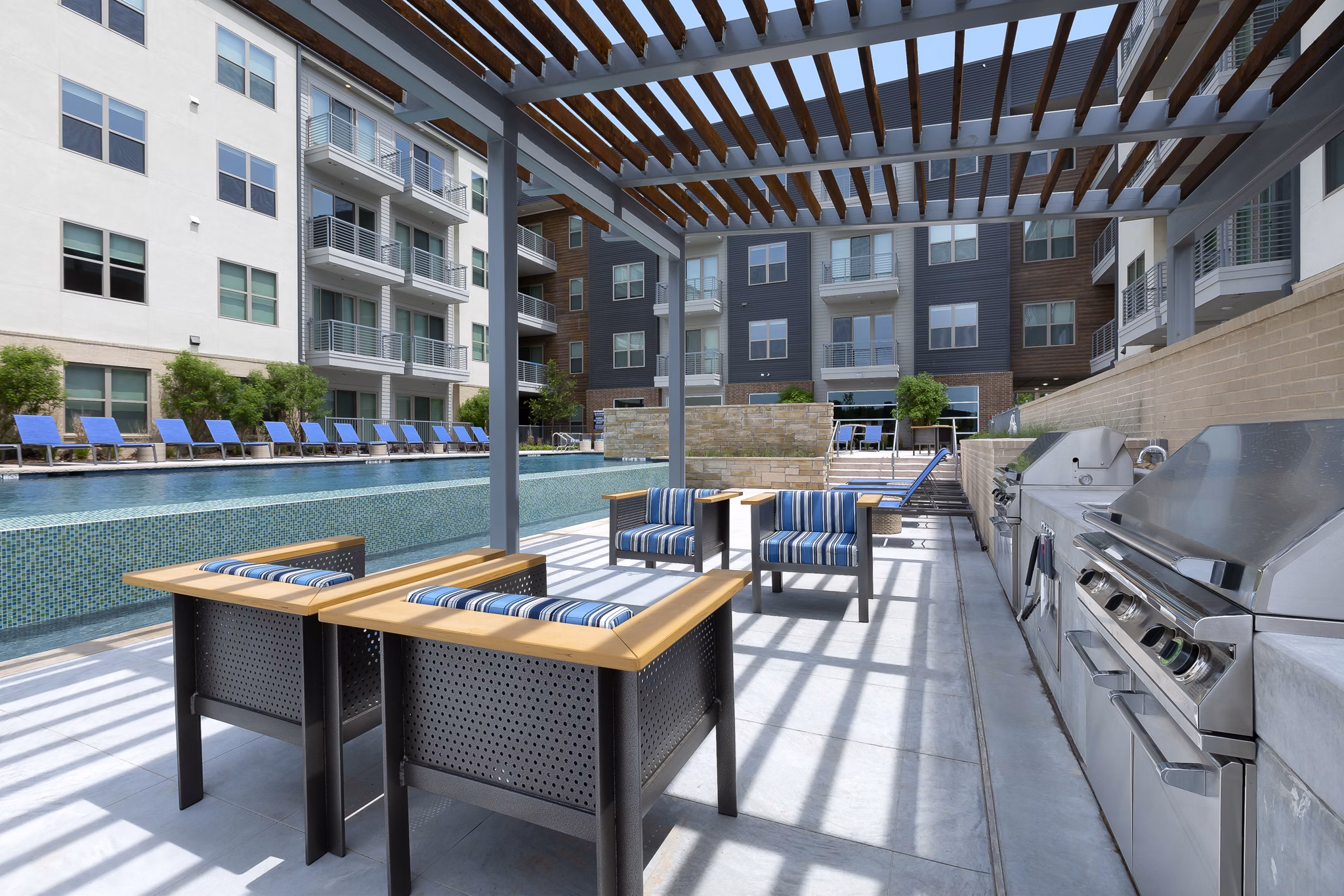 Stylish outdoor grill area at Atlas Waterside Apartments with modern seating and lush greenery, perfect for social gatherings