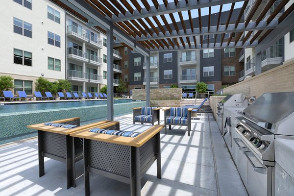 Stylish outdoor grill area at Atlas Waterside Apartments with modern seating and lush greenery, perfect for social gatherings