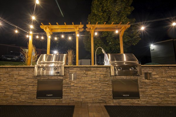Aspen Ridge Apartments: Modern outdoor grill area surrounded by lush greenery