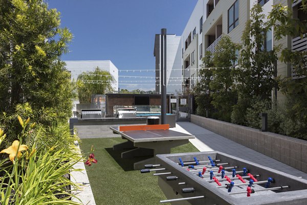 Outdoor recreational area with ping pong and foosball tables surrounded by greenery and seating at luxury apartments